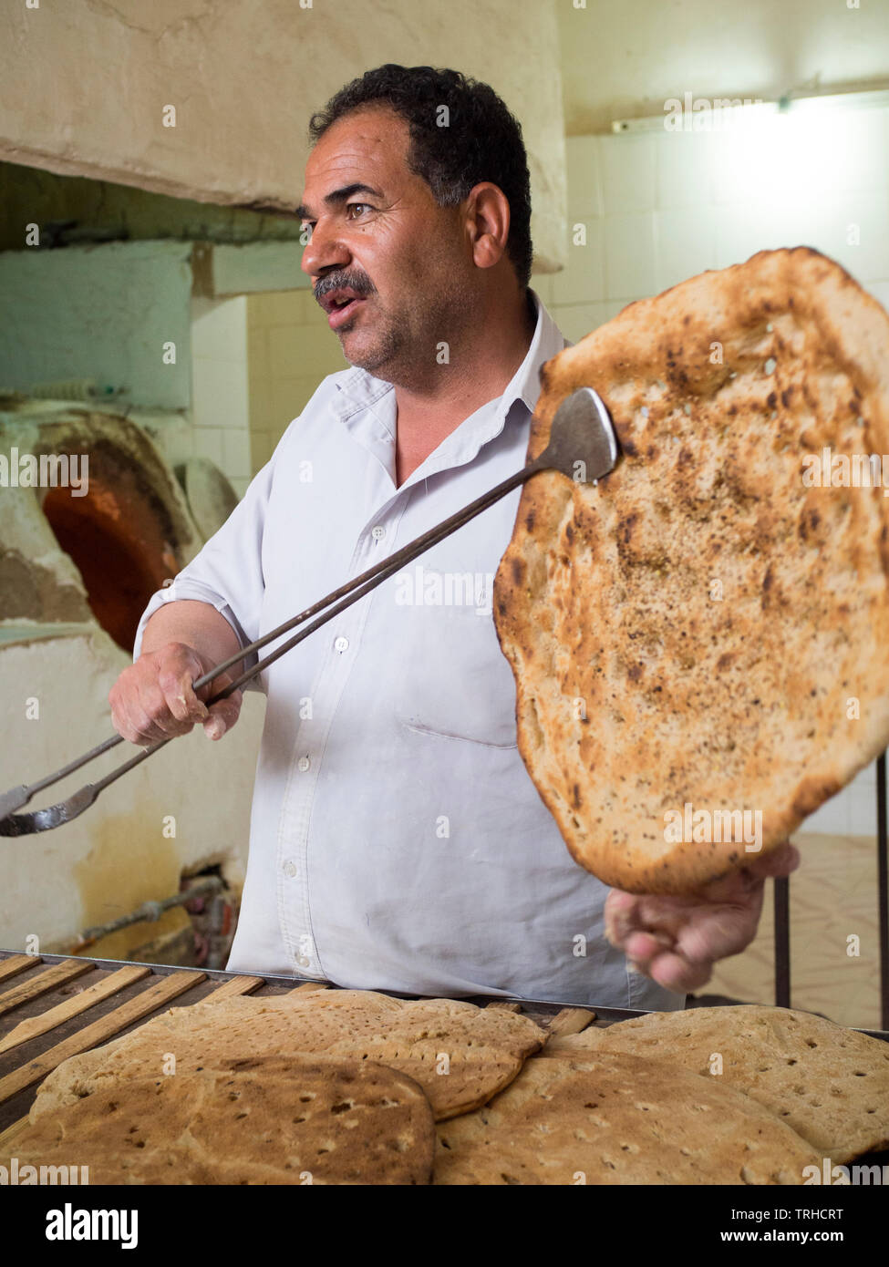 Ein Bäcker hält ein Stück frisches Naan Brot, ungesäuertes Brot in einem Ton Holz befeuerten Ofen, in Aqda, Iran. Stockfoto