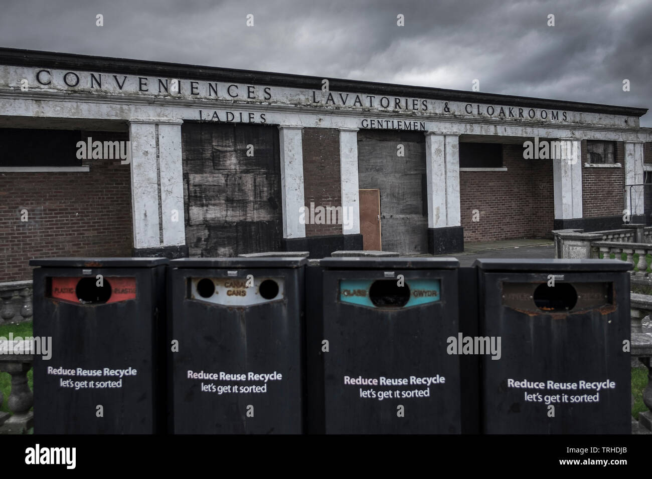 Eine verlassene wc Block, verfallende mit dem Alter, mit vier Recycling bins im Vordergrund, auch in schlechtem Zustand, in Barry Island, Barry, Wale entfernt Stockfoto