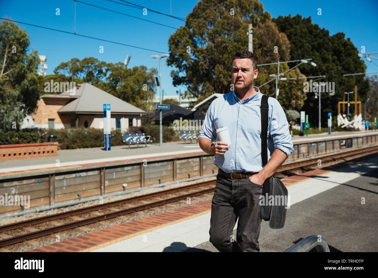 Eine Frontansicht Schoß eines Erwachsenen kaukasischen Geschäftsmann auf einem Bahnhof Plattform mit einer Tasse Kaffee in der Hand, er zieht das t Stockfoto