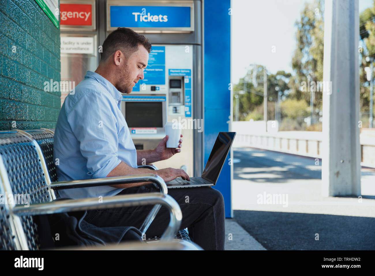 Eine Seitenansicht Schoß eines Erwachsenen kaukasischen Geschäftsmanns, der auf seinem Laptop, während er wartet darauf, dass der Zug an einem Bahnhof Plattform, Stockfoto