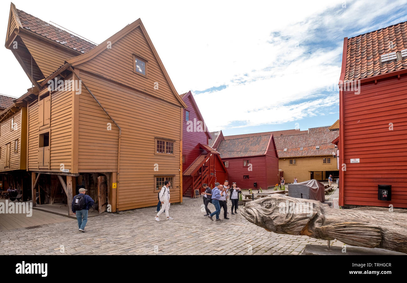 Große, hölzerne Fisch Denkmal auf einem gepflasterten Weg auf die Touristen zu Fuß durch die schöne Holzhäuser in Bryggen, Bergen, Hordaland, Norwegen, Sc umgeben Stockfoto