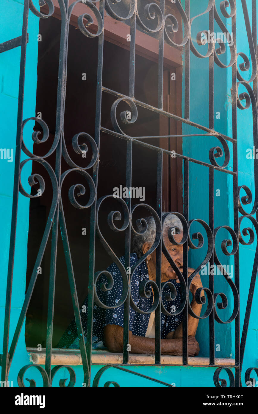 Ältere Dame suchen durch die Bars außerhalb ihres Fensters in einem traditionellen Haus in der UNESCO-Stadt Trinidad, Kuba, Karibik Stockfoto