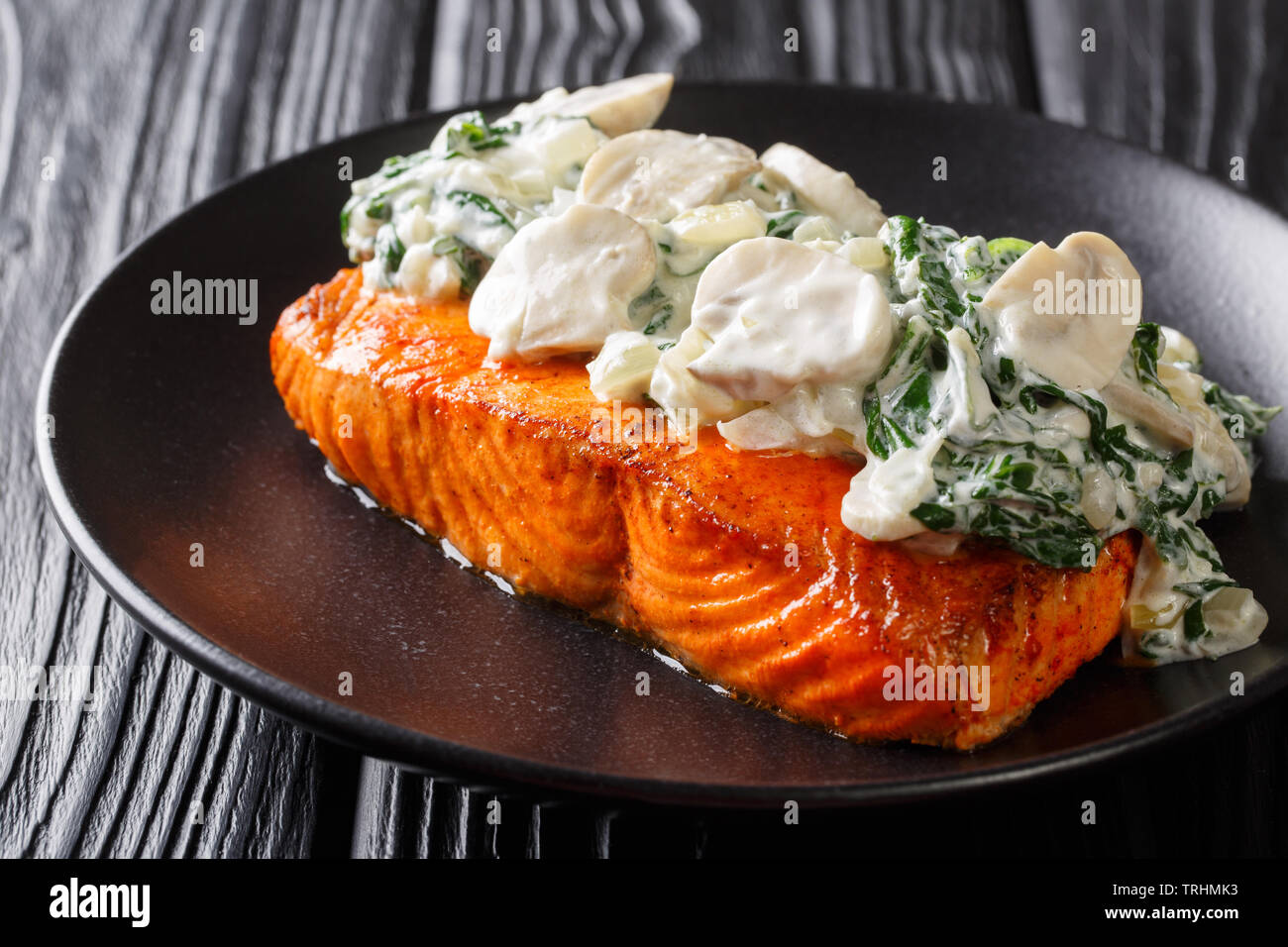 Gebackene Florentiner Lachs mit cremiger Wein Sauce, gewürzt mit gebratener Spinat und Pilze auf einem Teller auf den Tisch closeup. Horizontale Stockfoto