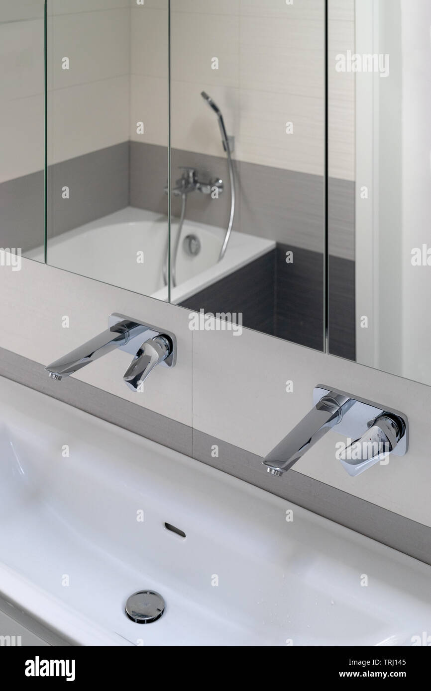 Detail der modernen Bad. Waschbecken mit zwei Hähne und Spiegel. Das Bad mit Dusche ist in ihm reflektiert. Stockfoto