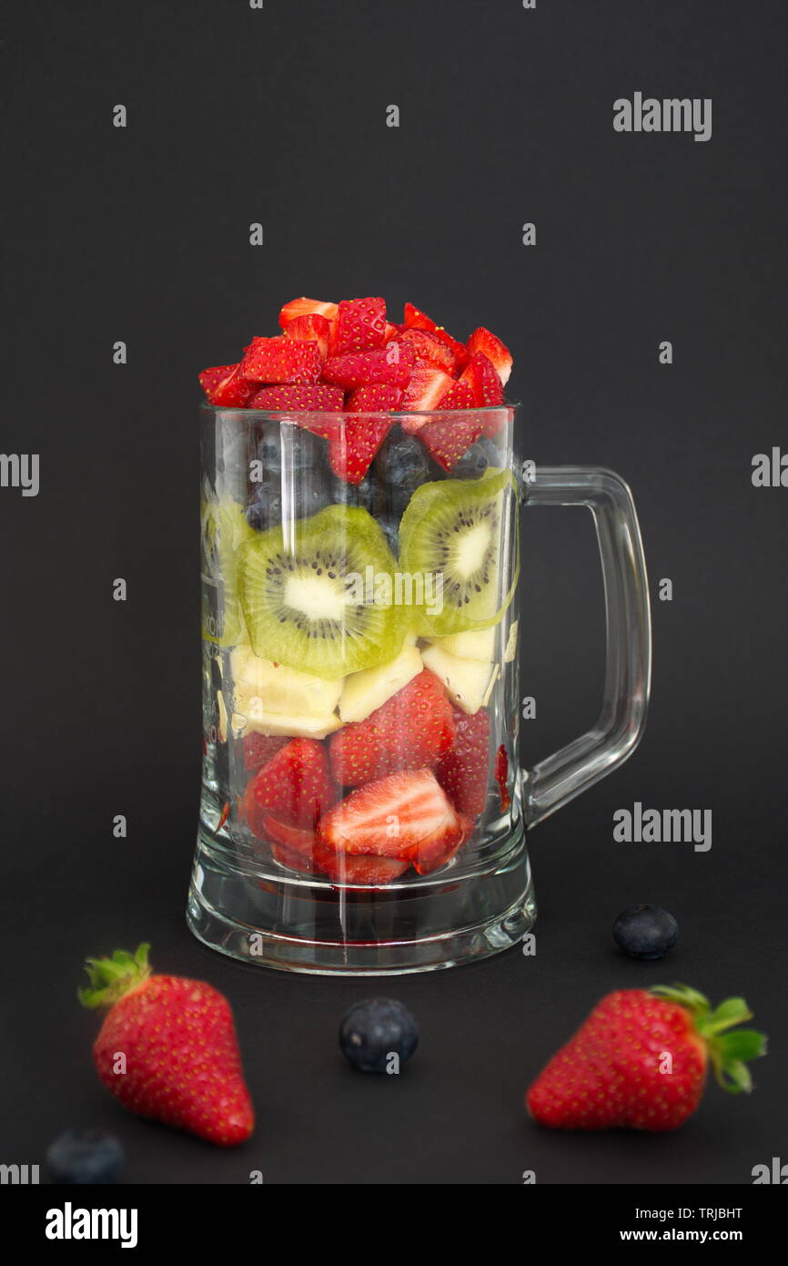 Beerenfrucht, Apple und Kiwi schneiden und in das Glas gegen den schwarzen Hintergrund Stockfoto