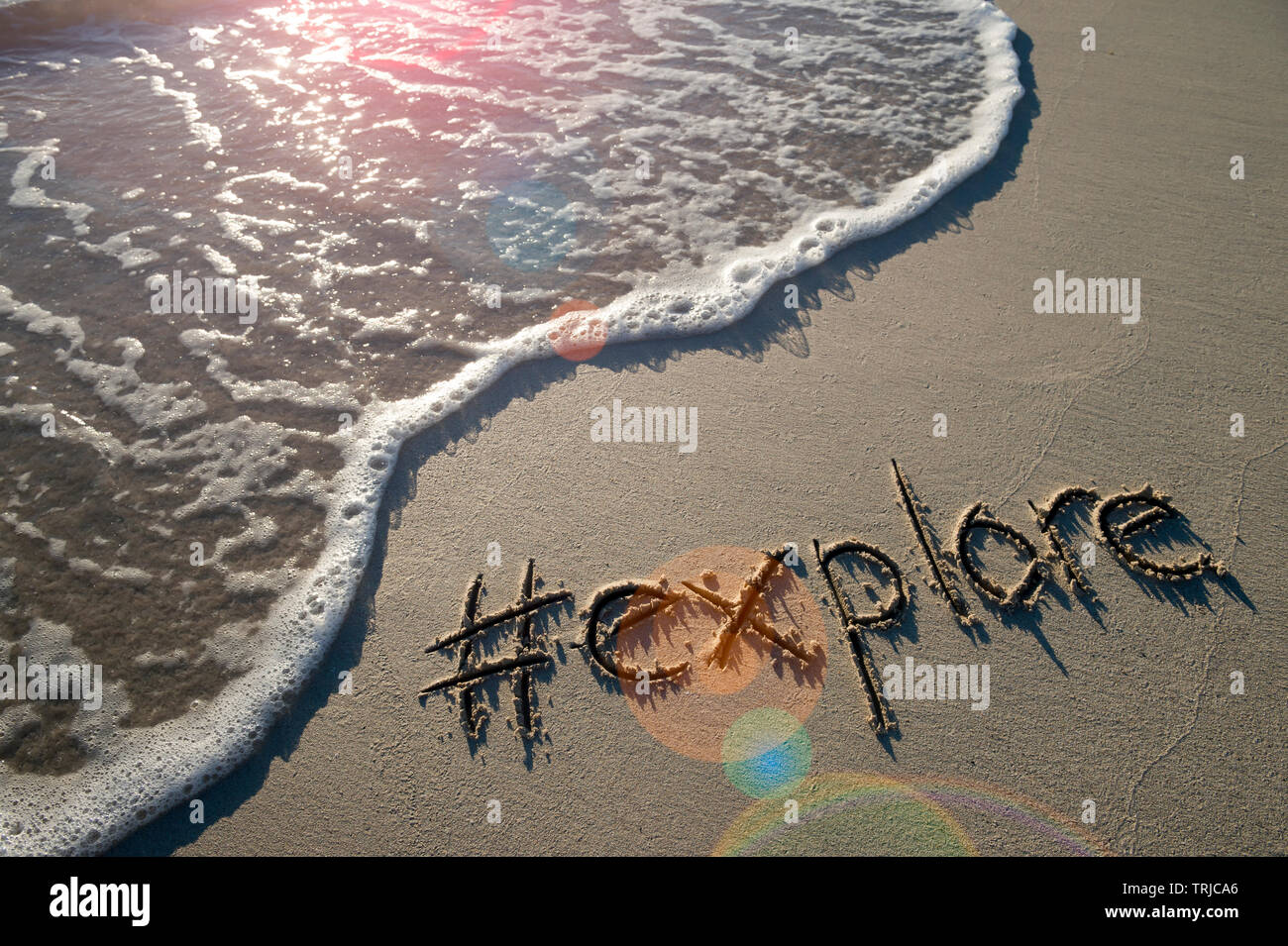 Modernes reisen Nachricht für den Strand mit einem Social Media - freundliche Hashtag geschrieben mit dem Wort in glatten Sand mit ankommenden Welle erkunden Stockfoto