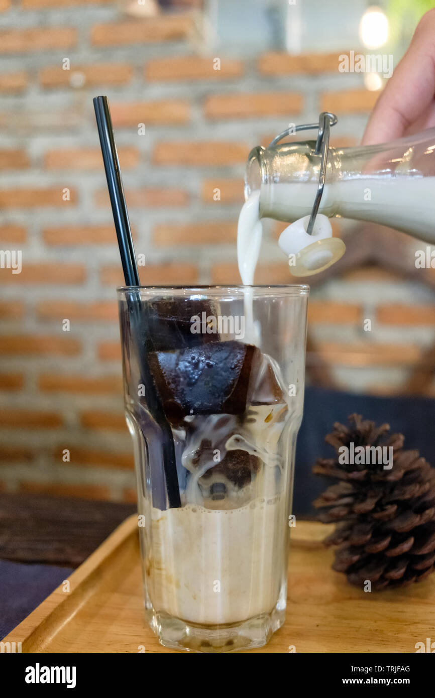 Eis Kaffee Cubes mit Milch Gießen in Glas in Retro Cafe Stockfoto