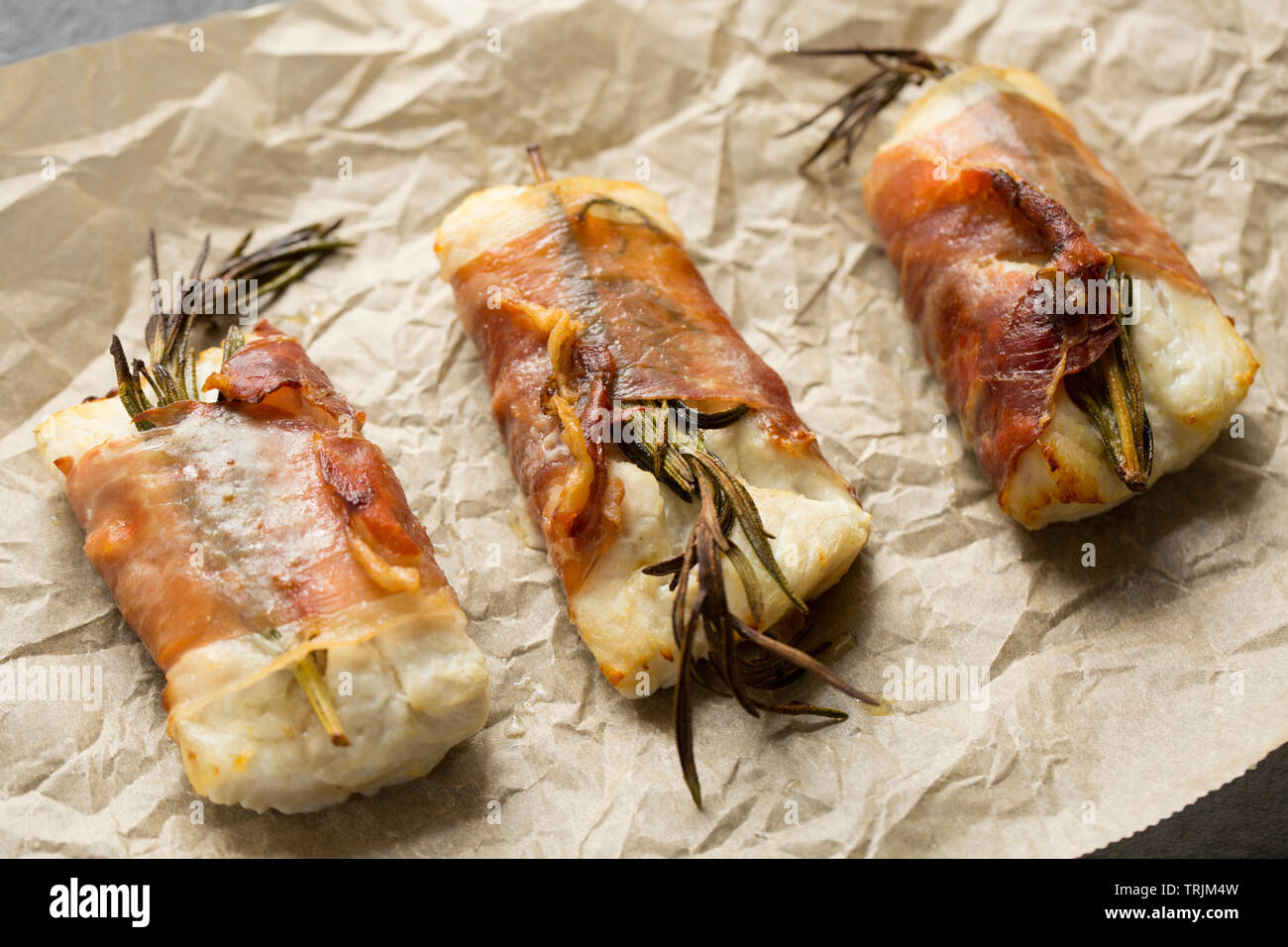 Drei gekocht Filets von Pollack Pollachius pollachius, dass in Zitronensaft und zerdrückten Knoblauch, bevor in Parmaschinken w eingewickelt zu werden, mariniert worden sind Stockfoto