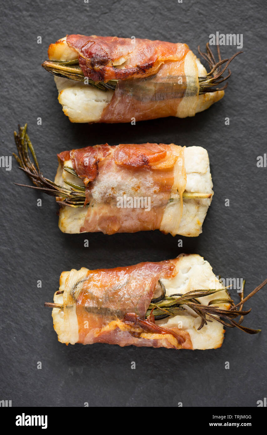 Drei gekocht Filets von Pollack Pollachius pollachius, dass in Zitronensaft und zerdrückten Knoblauch, bevor in Parmaschinken w eingewickelt zu werden, mariniert worden sind Stockfoto