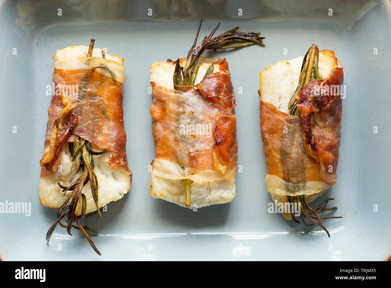 Drei gekocht Filets von Pollack Pollachius pollachius, dass in Zitronensaft und zerdrückten Knoblauch, bevor in Parmaschinken w eingewickelt zu werden, mariniert worden sind Stockfoto