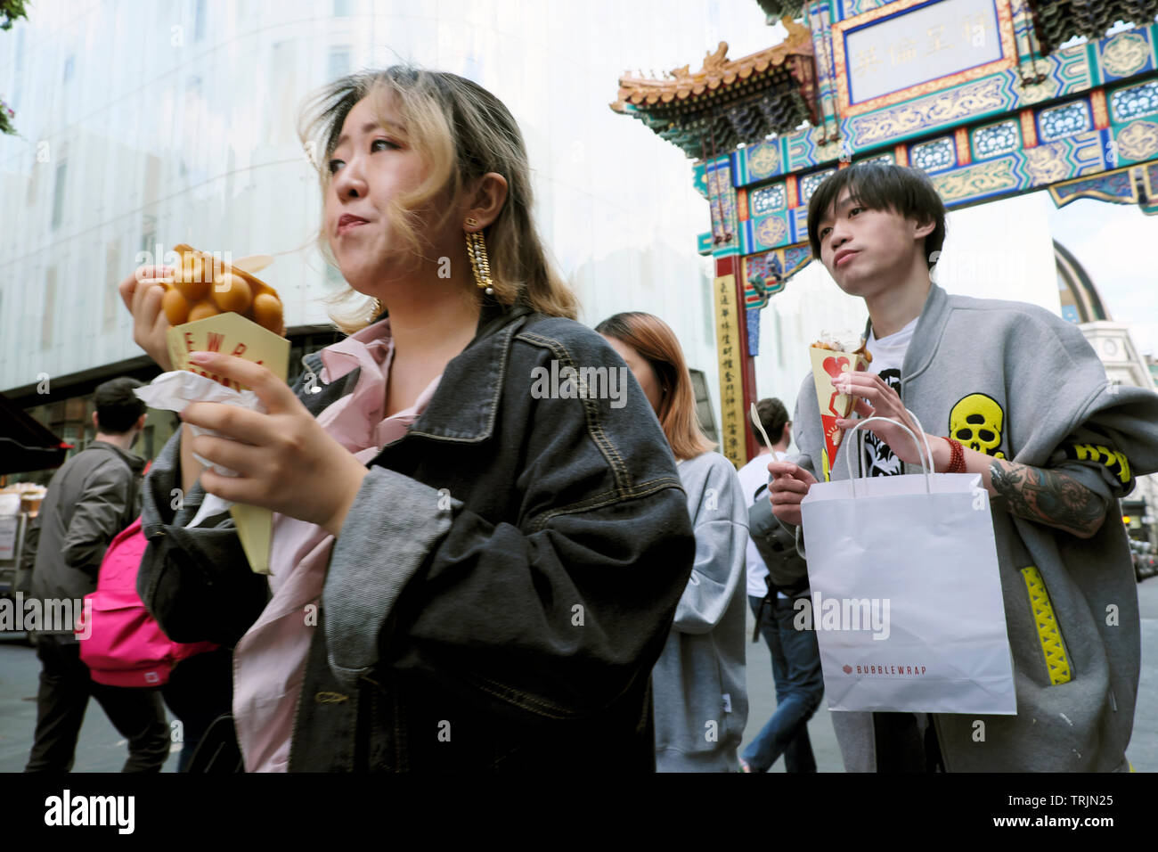 Trendige junge Leute, die auf der Wardour Street spazieren gehen und Essen aus dem Bubblewrap Waffelladen und der Tragetasche in Chinatown London W1 England KATHY DEWITT essen Stockfoto