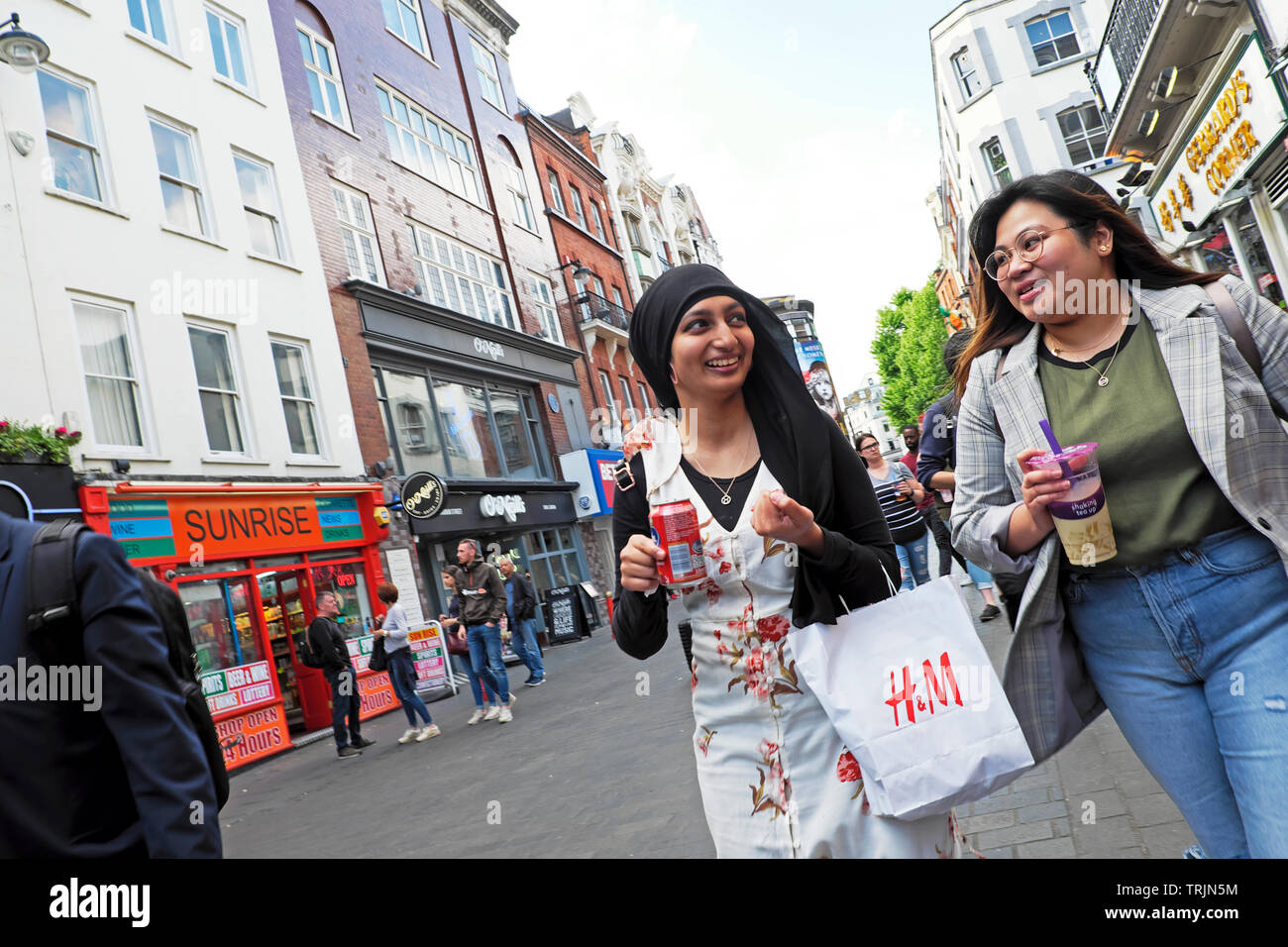 Junge Frauen gehen, reden und shoppen mit H&M Einkaufstasche auf der Gerrard Street in Chinatown London W1 England Großbritannien KATHY DEWITT Stockfoto
