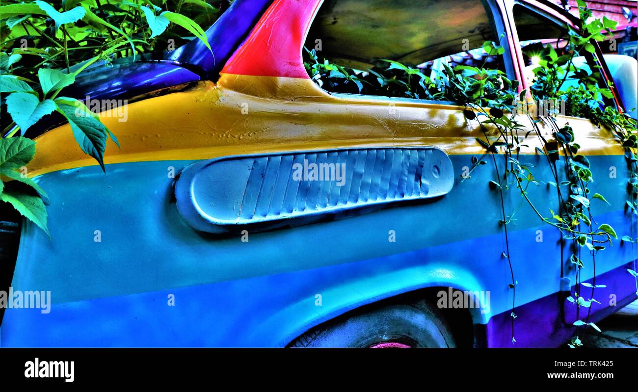 Eine alte italienische Fiat 500 Auto in Regenbogenfarben bemalt, in Kletterpflanzen bedeckt, auf einem Bürgersteig geparkt. Stockfoto