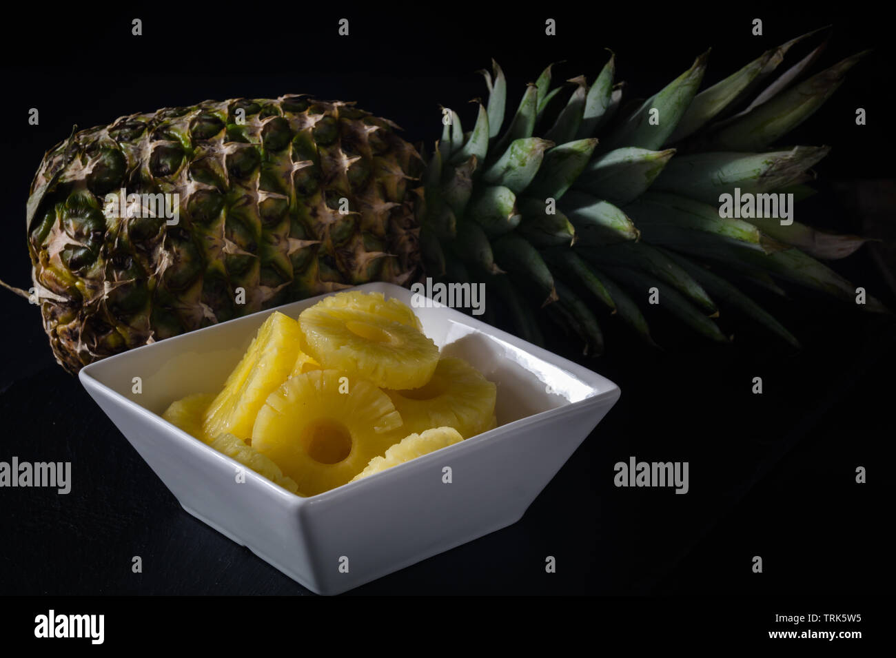 Ananas auf schwarzen Hintergrund. Mit runden reifen Stücke Ananas in einer weißen Schüssel. Stockfoto