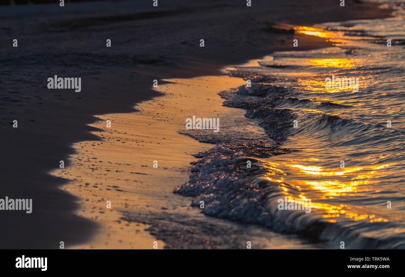 Die Wellen am Strand brechen. Schönen Sonnenuntergang mit goldenem Licht spiegelt sich im Wasser. Stockfoto