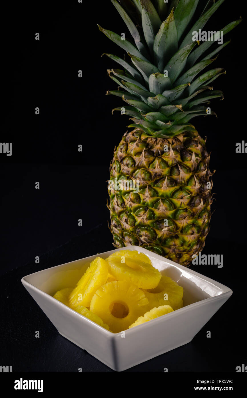Ananas auf schwarzen Hintergrund. Mit runden reifen Stücke Ananas in einer weißen Schüssel. Stockfoto