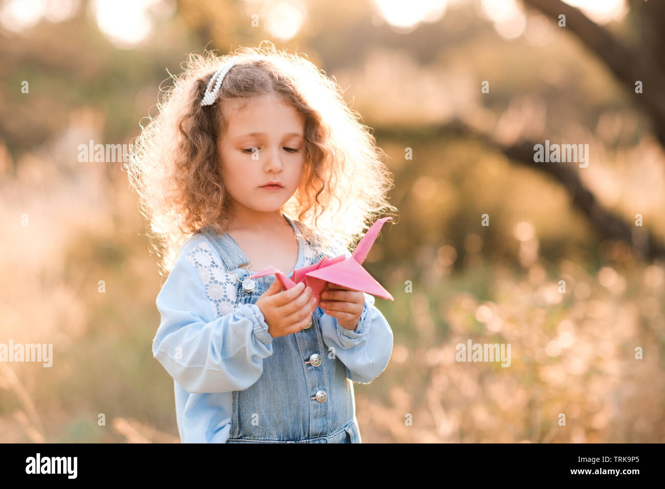 Süße blonde Kind Mädchen 3-4 Jahre alten Holding Papier origami Crane  stehen draußen über die Natur Hintergrund. Kinder spielen mit Spielzeug.  Kindheit Stockfotografie - Alamy