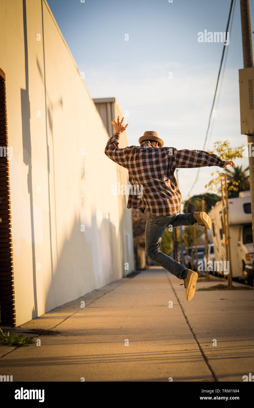 Ein kaukasischer Mann freudig Springen auf einer Straße, Bürgersteig, der mit dem Rücken zur Kamera. Ein fröhliches Konzept! Stockfoto