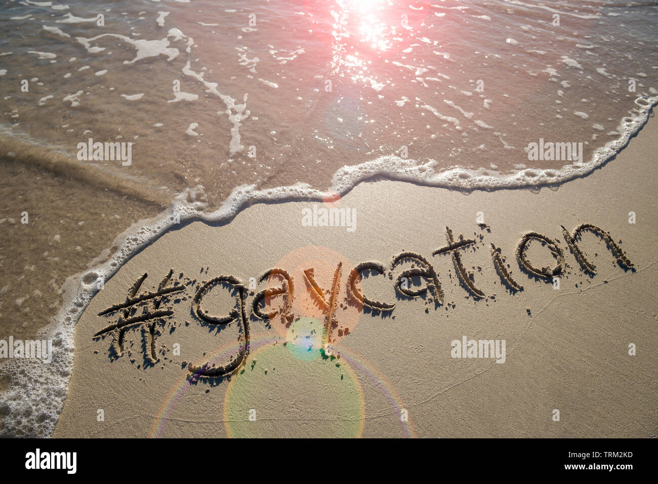 Moderne gay-friendly travel Meldung 'gaycation' mit einem Social Media - freundliche hashtag in glatten Sand geschrieben mit ankommenden Welle auf den Strand Stockfoto