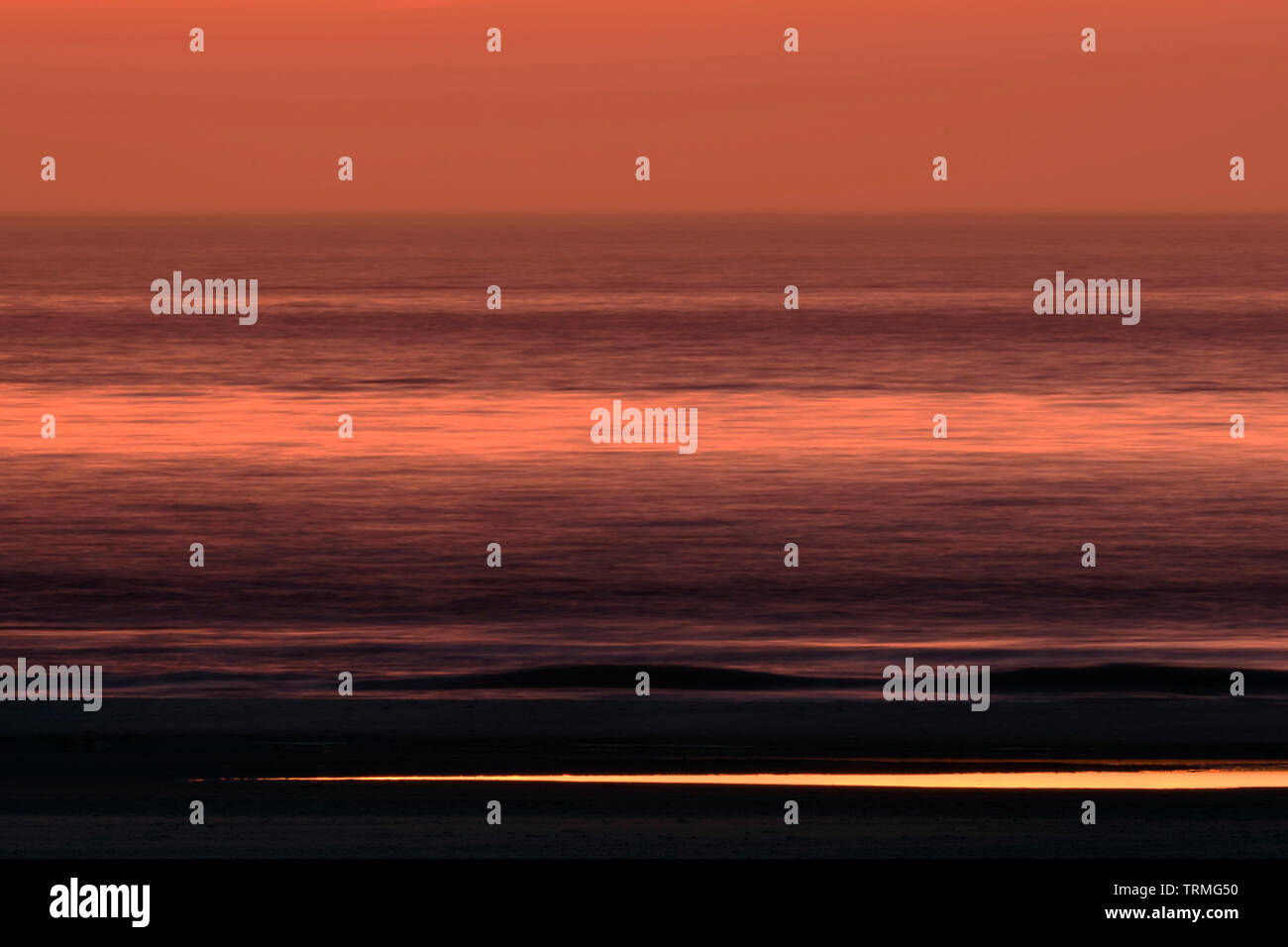 Lange Exposition der rot gefärbten Himmel, Meer und Strand nur wenige Minuten nach Sonnenuntergang, Morgengrauen, voller Atmosphäre und Stille, Europa verwischt. Stockfoto