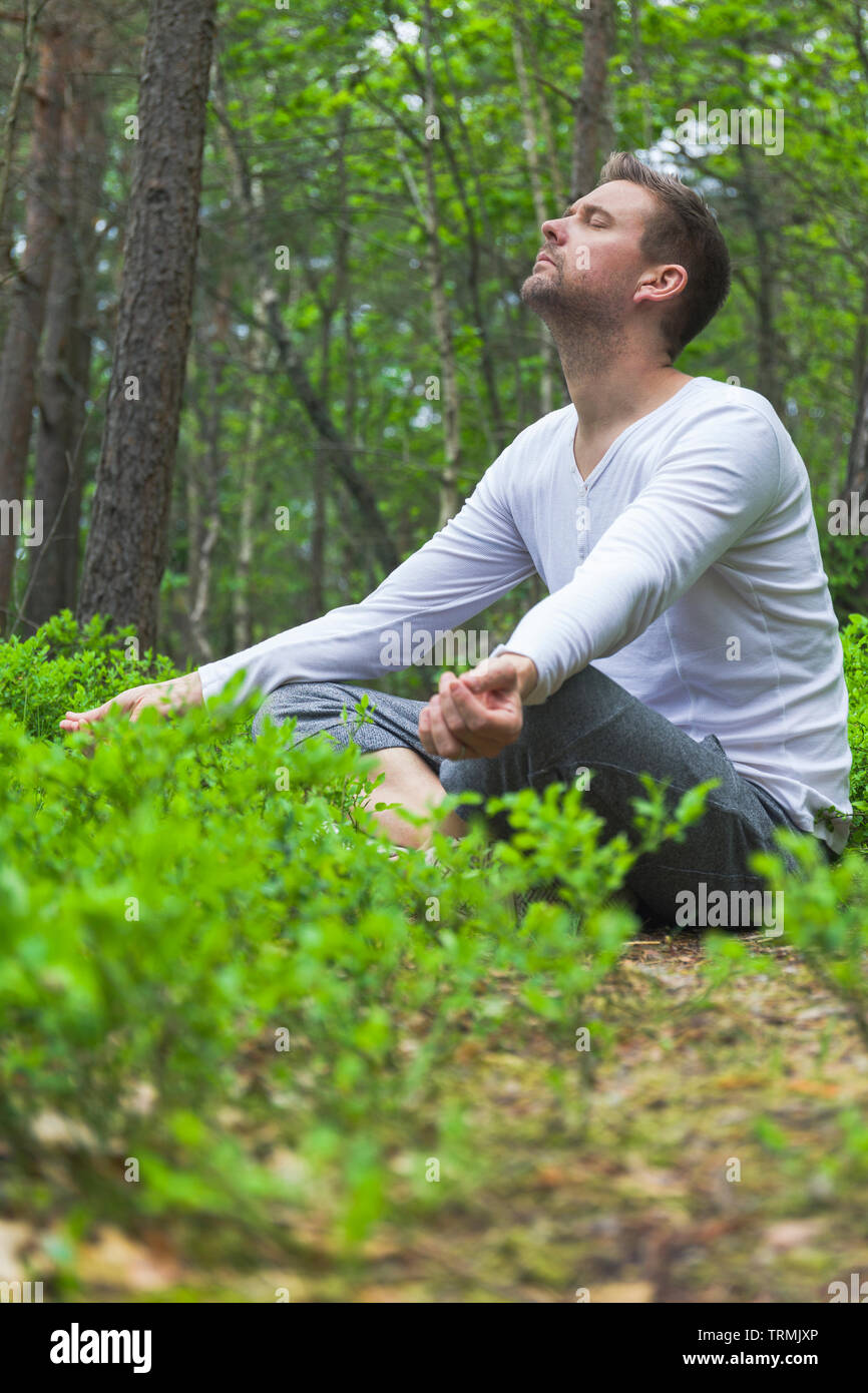 Mitte nach kaukasischer Mann sitzen draußen allein mit geschlossenen Augen meditieren in einem üppigen grünen Wald in typisch entspannten Pose Stockfoto