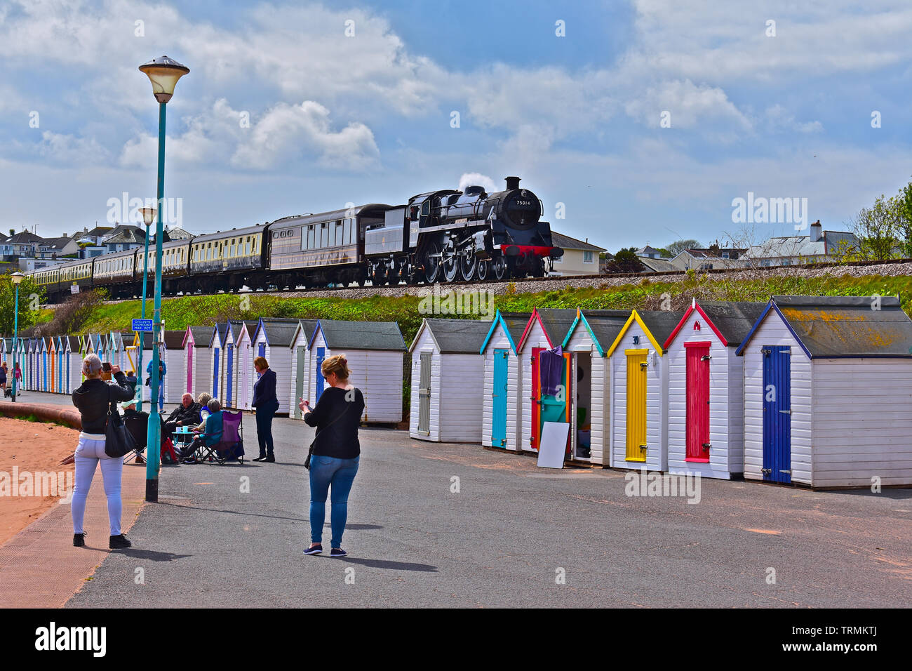 Motor Nr. 75015 'Braveheart' des Dartmouth Steam Railway, in Goodrington station dampft, vorbei an einer Reihe von bunten Badekabinen. Stockfoto