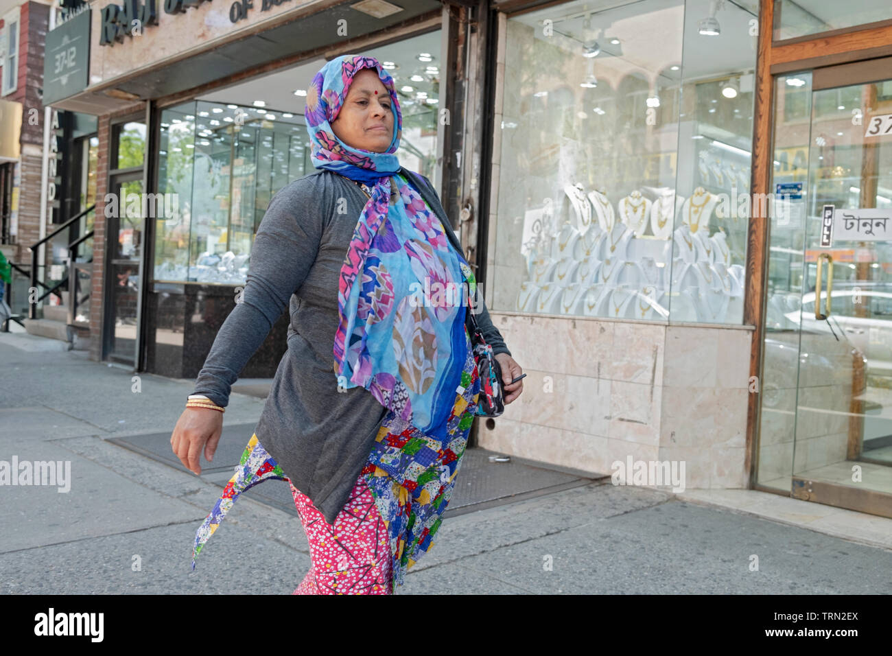 Eine Frau in einem bunten Kleid und Kopfbedeckung Spaziergänge auf 74th Street in Jackson Heights in ihren Gedanken versunken. Queens, New York City. Stockfoto