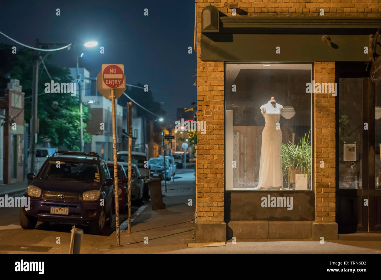 Geparkte Autos und ein Brautkleid in einem Schaufenster in der Nacht in der Nähe von Brunswick Street, Fitzroy, Victoria, Australien Stockfoto