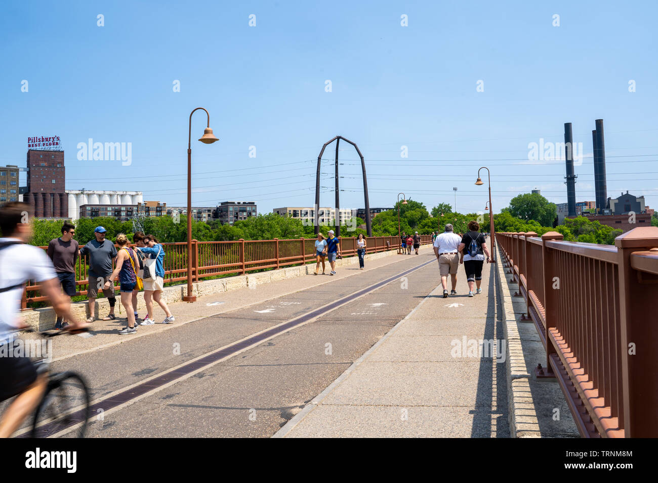 Minneapolis, Minnesota - Juni 1, 2019: Fußgänger und Radfahrer einen schönen Frühlingstag genießen Sie einen Spaziergang über die steinerne Bogenbrücke im St. Anthony Falls Stockfoto