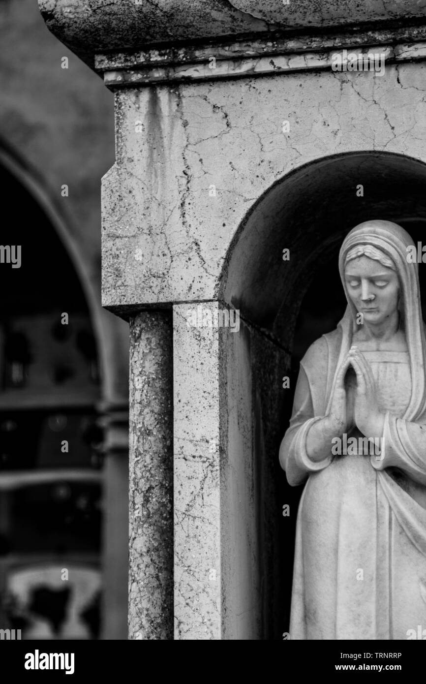 Die Statue einer Frau in Granit hat ihre Hände gekreuzt und betet in der kleinen Kirche auf dem Friedhof von Parma. Stockfoto