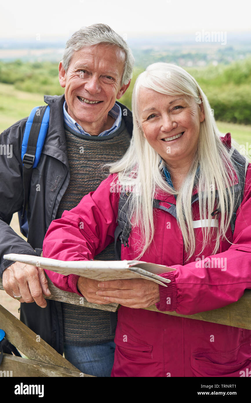 Portrait von lächelnden Senior Paar mit Karte Wandern in der Landschaft stehend von Gate Stockfoto