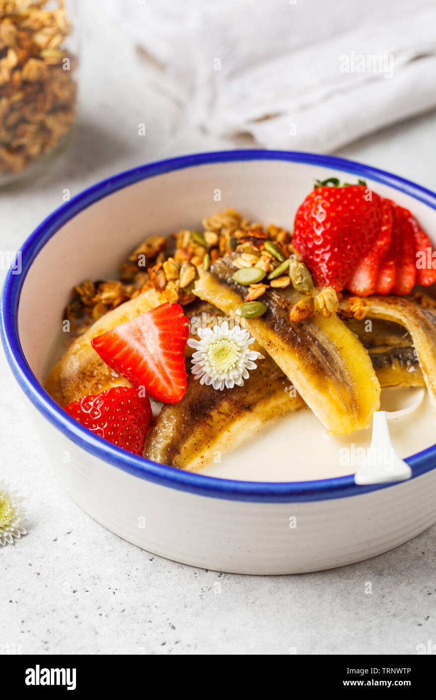 Hausgemachtes Müsli mit Erdbeeren und gebratenen Bananen in einer weißen Schüssel. Stockfoto