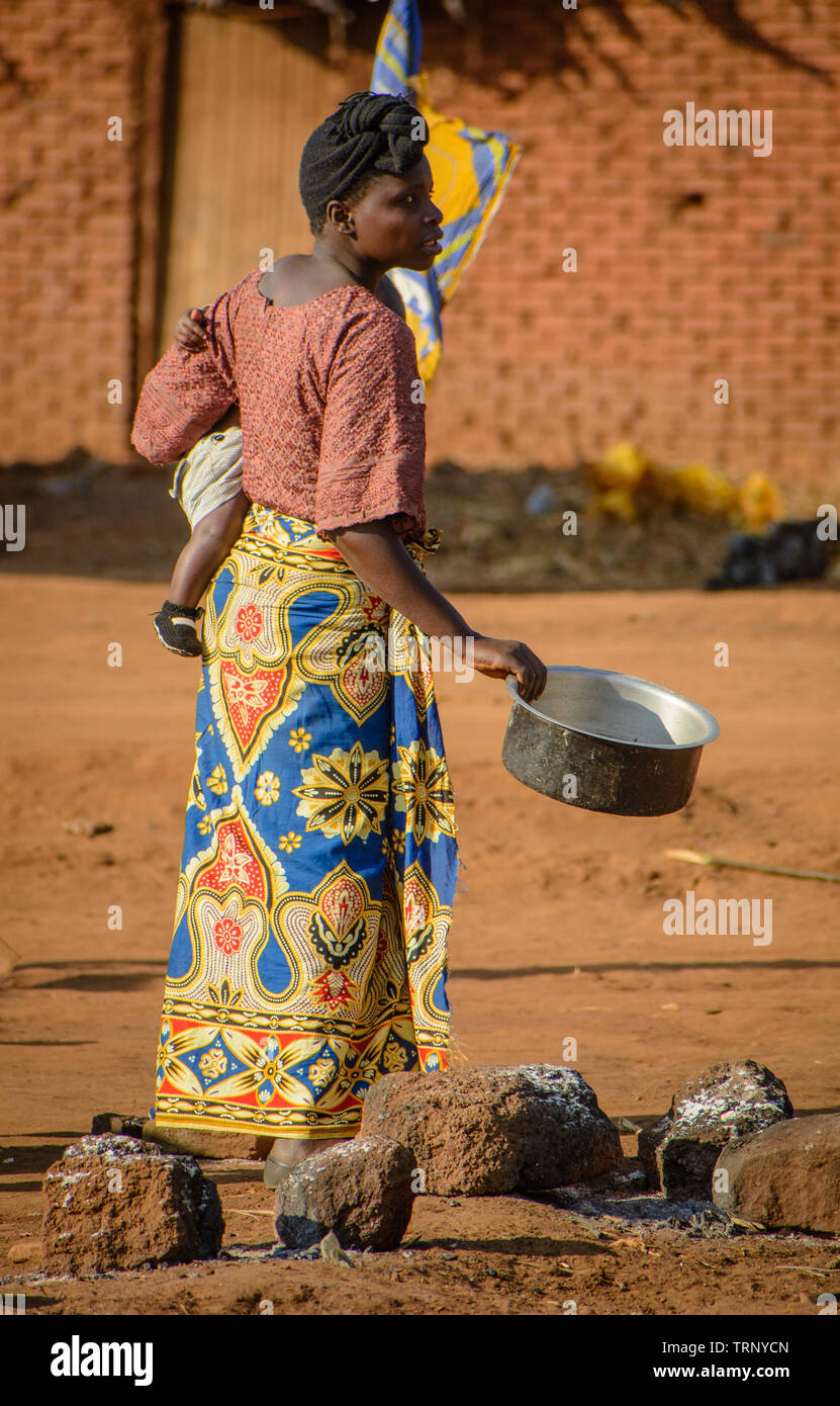 Malawische Frau ihr Baby an ihrer Hüfte und einem Kochtopf in der Hand hält, eine andere Frau zu sprechen Stockfoto