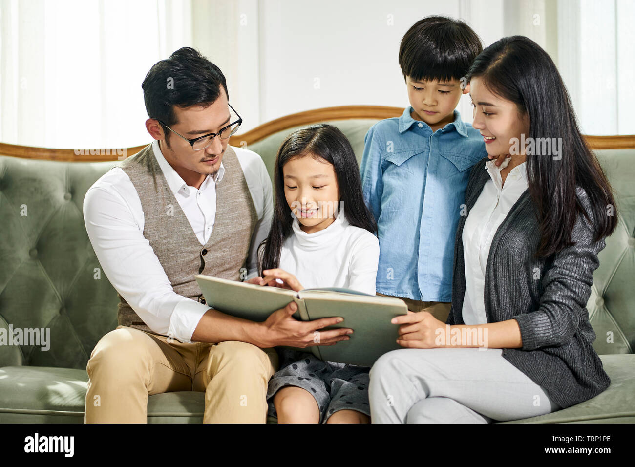 Asiatische Eltern und zwei Kinder zusammen auf der Couch lesen Buch zu Hause sitzen Stockfoto