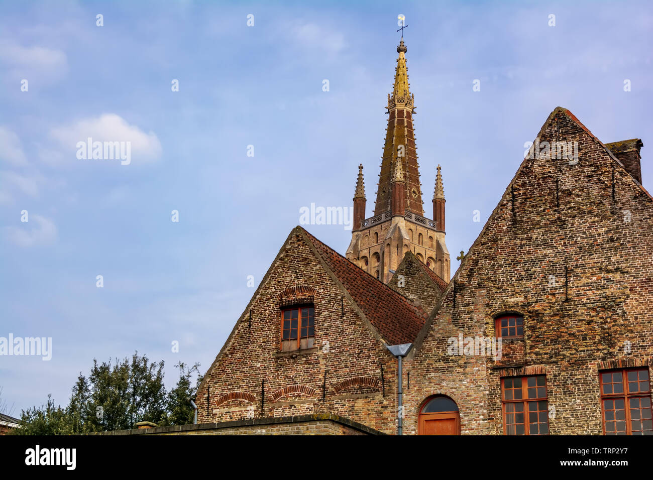 Die Kirche Unserer Lieben Frau (Onze-Lieve-Vrouwekerk) Tower hinter mittelalterlichen Häusern gegen den blauen Himmel gesehen. Dieses gotische Turm ist 122,3 Meter hoch Stockfoto