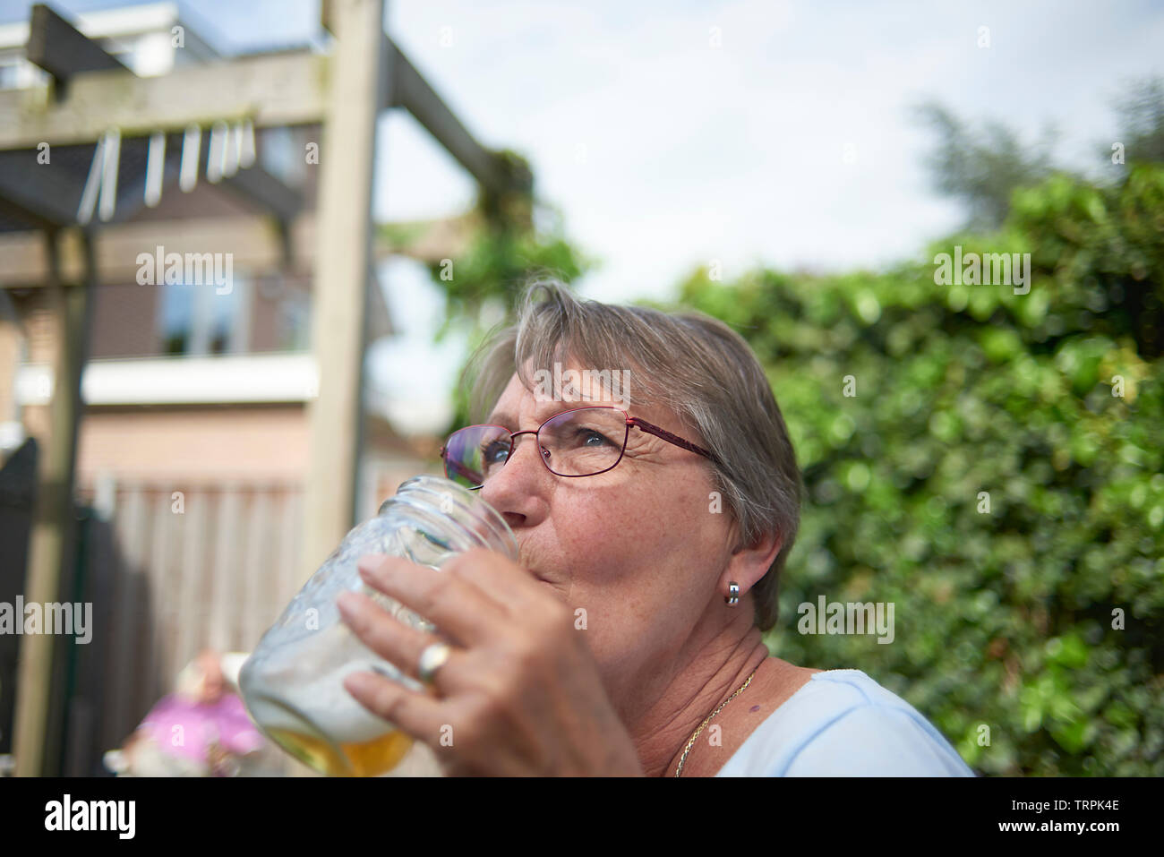 Glückliche und Gesunde ältere Frau trinkt ein großes Glas Bier draußen im hellen Sommer Sonnenschein Stockfoto