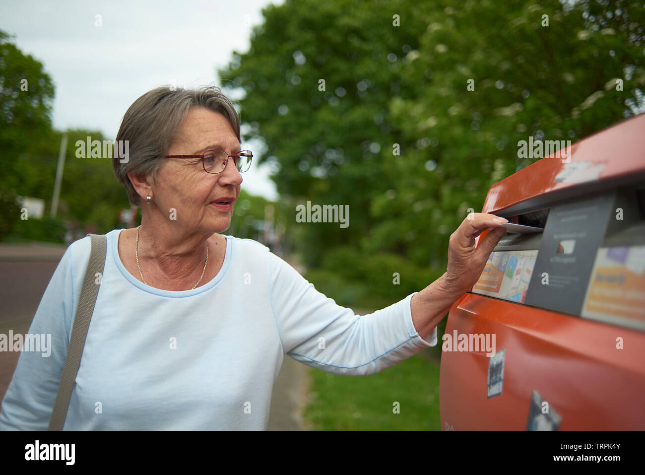 Glückliche und Gesunde ältere Frau, einen Brief in einen roten Briefkasten draußen im hellen Sommer Sonnenschein Stockfoto