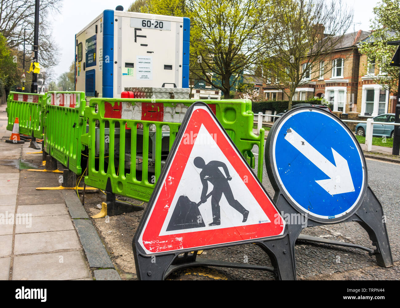 "Bei der Arbeit" und "Rechts halten" Zeichen vor den Baustellen, durch helle grüne Barrieren umgeben. Ealing, London W5, England, UK. Stockfoto