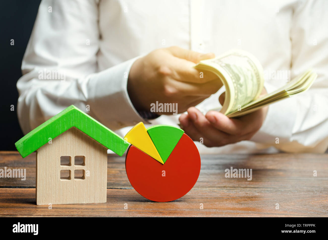 Ein Miniatur Holzhaus und ein Kreisdiagramm. Geschäftsmann zählt Geld. Konzept der real estate Marktanalyse und Analytics. Segmentierung und Marketing. Stockfoto