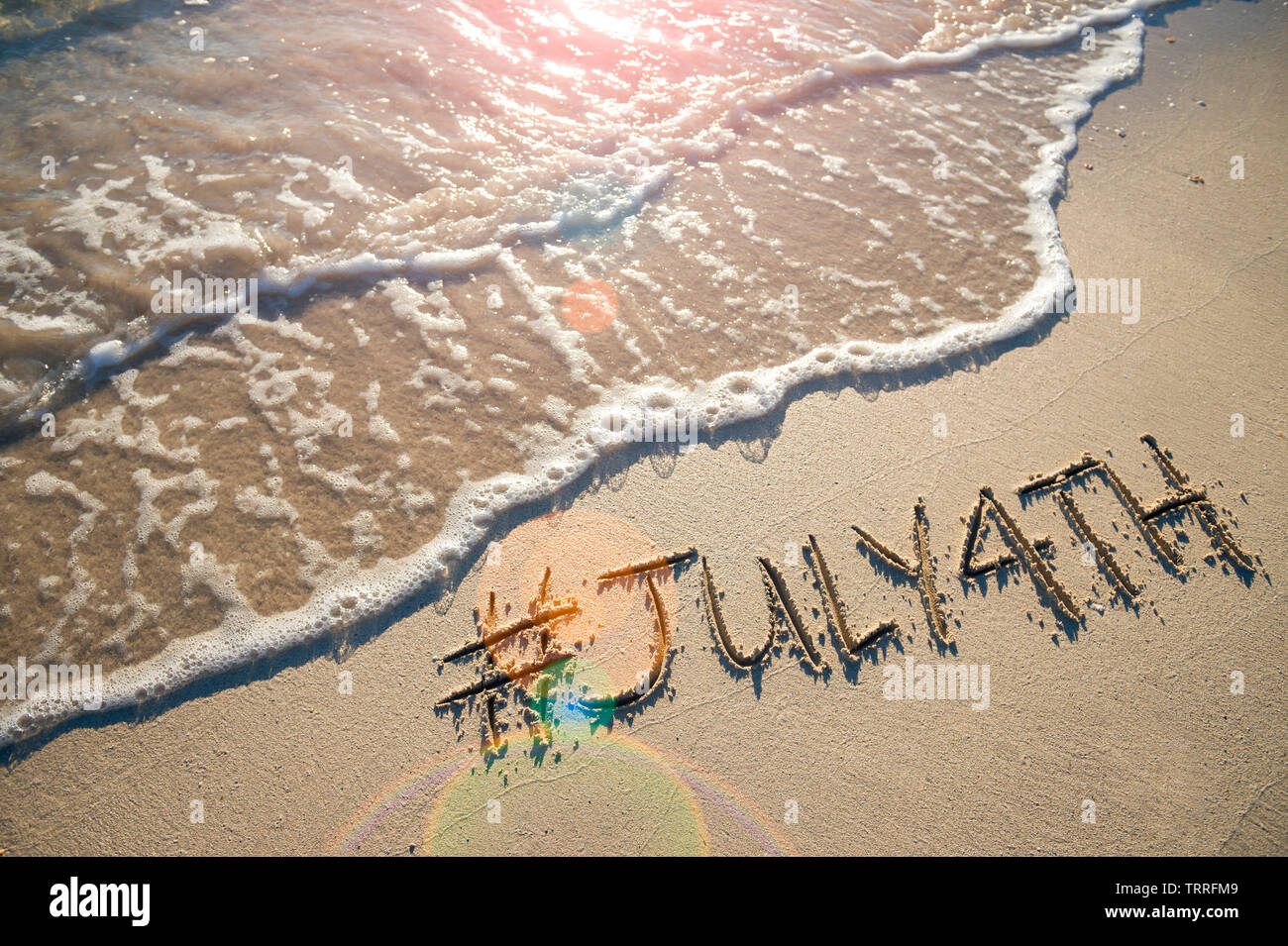 Moderne Nachricht für den 4. Juli amerikanischen Feiertag mit einem Social Media - freundliche hashtag in glatten Sand geschrieben mit ankommenden Welle auf den Strand Stockfoto