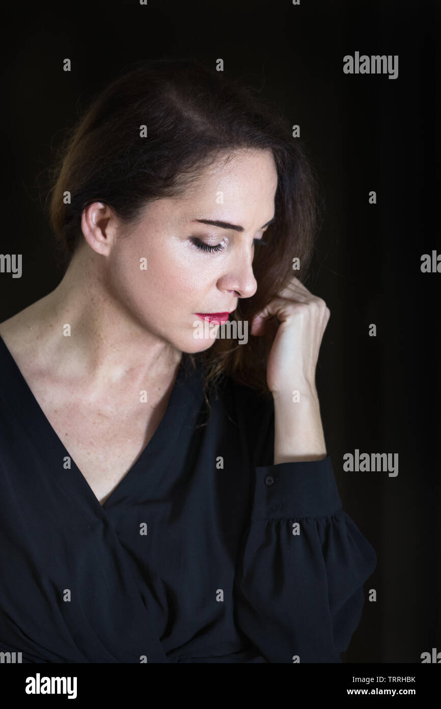 Porträt einer Frau, die 48 Jahre alt, auf der Suche nach duftenden ihr Handgelenk mit geschlossenen Augen, über Schwarz, Low Key Beleuchtung isoliert. Stockfoto