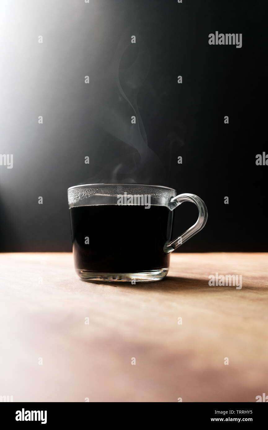 Hot Steamy Glas Kaffeetasse mit kopieren. Steamy Glas Tasse mit schwarzem Kaffee auf einem schwarzen Hintergrund dargestellt. Stockfoto