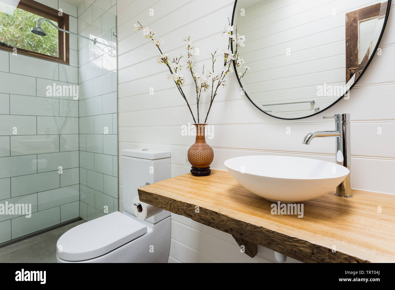 Badezimmer mit Waschbecken, Holzbank, runde, schwarze Spiegel und Dusche Stockfoto