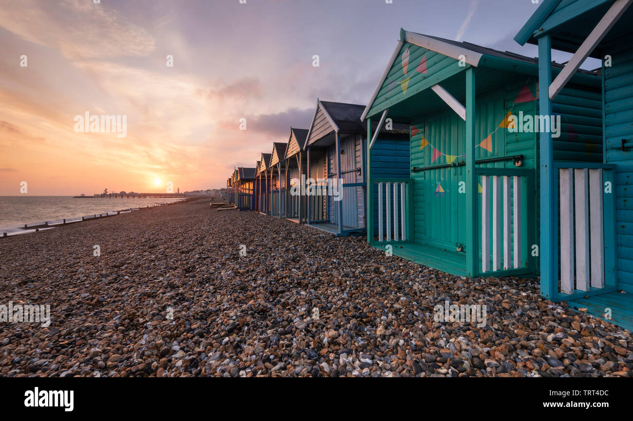 Bunte Badehäuschen in Herne Bay direkt am Meer wie die Sonne über dem historischen Pier. Stockfoto
