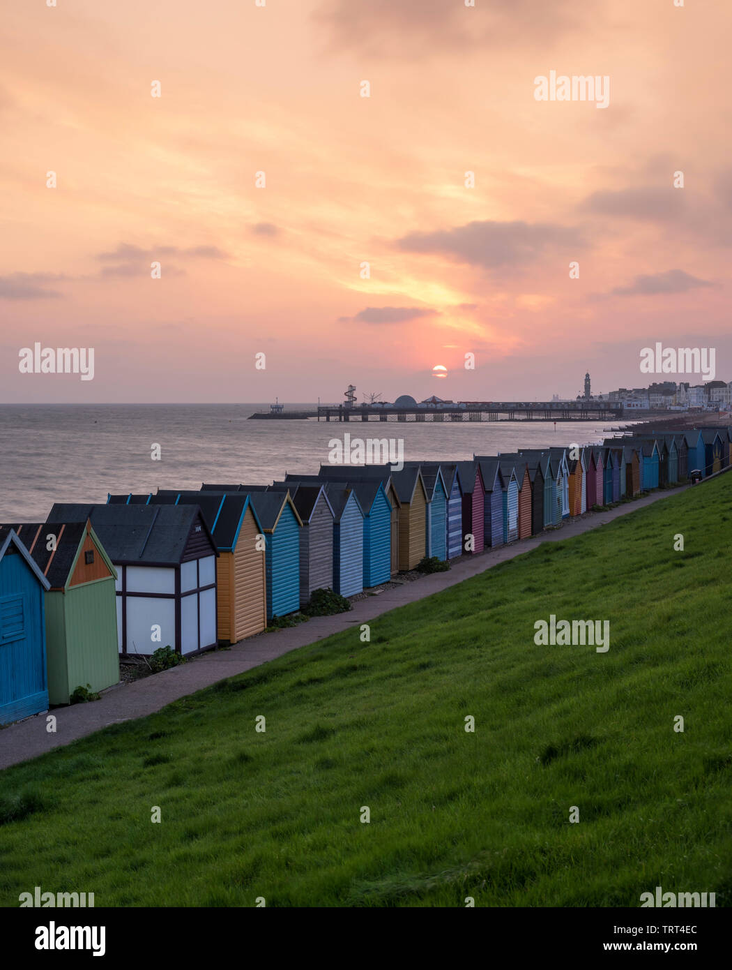 Bunte Badehäuschen in Herne Bay direkt am Meer wie die Sonne über dem historischen Pier. Stockfoto