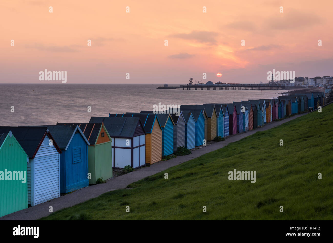 Bunte Badehäuschen in Herne Bay direkt am Meer wie die Sonne über dem historischen Pier. Stockfoto