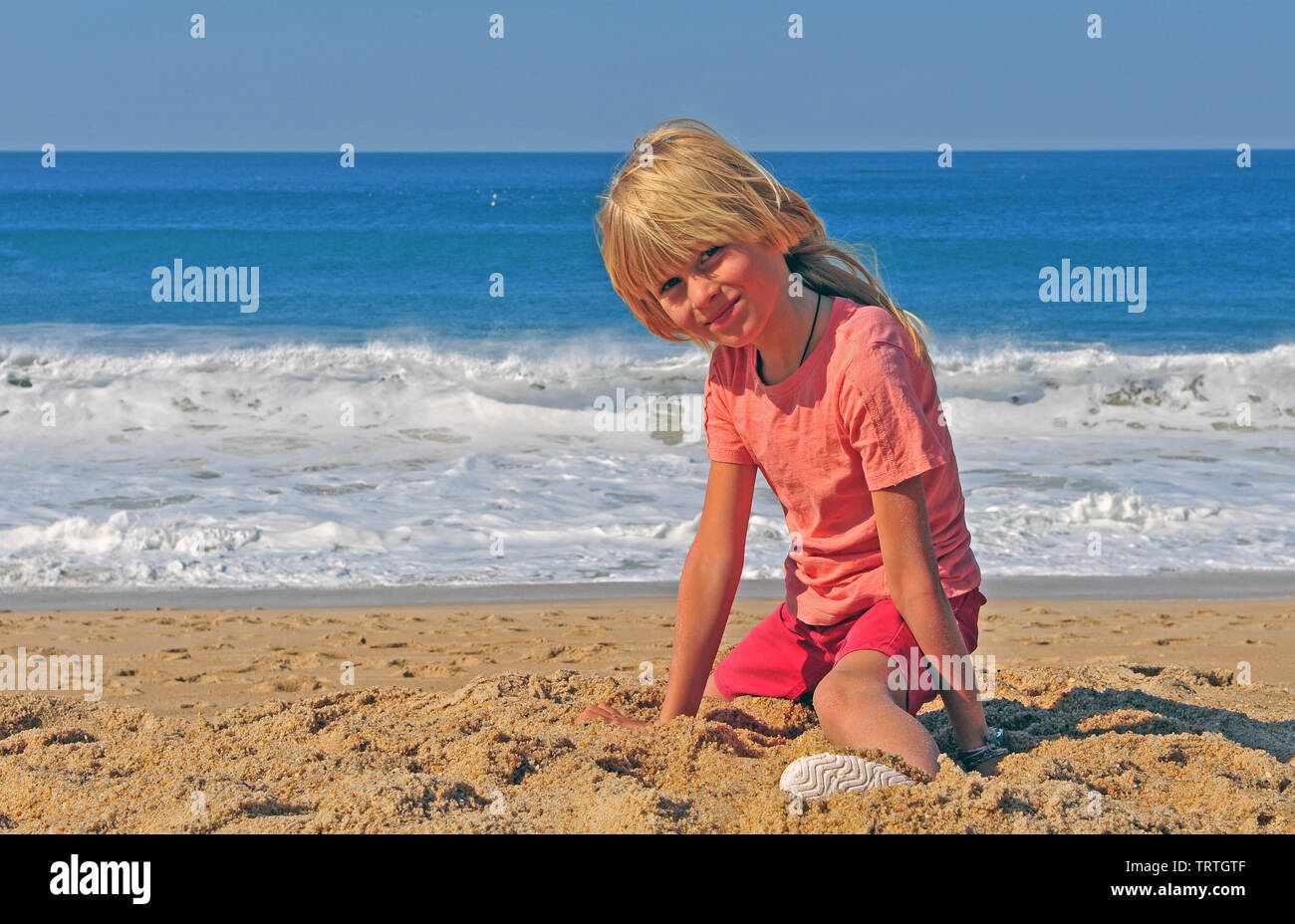 Lächelnde Junge sitzt am Strand mit Blick auf das Meer im Hintergrund Stockfoto