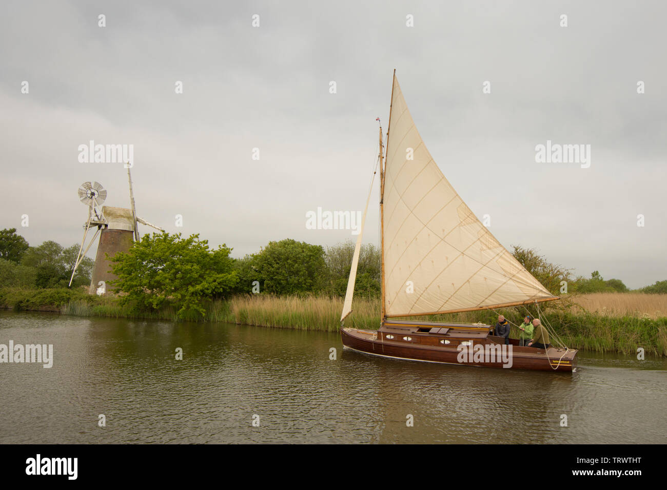 Drei Männer im Segelboot auf dem Fluss Ant Segeln vor Rasen Fen Entwässerung Mühle, wie Hügel, Norfolk Broads, UK, Mai Stockfoto