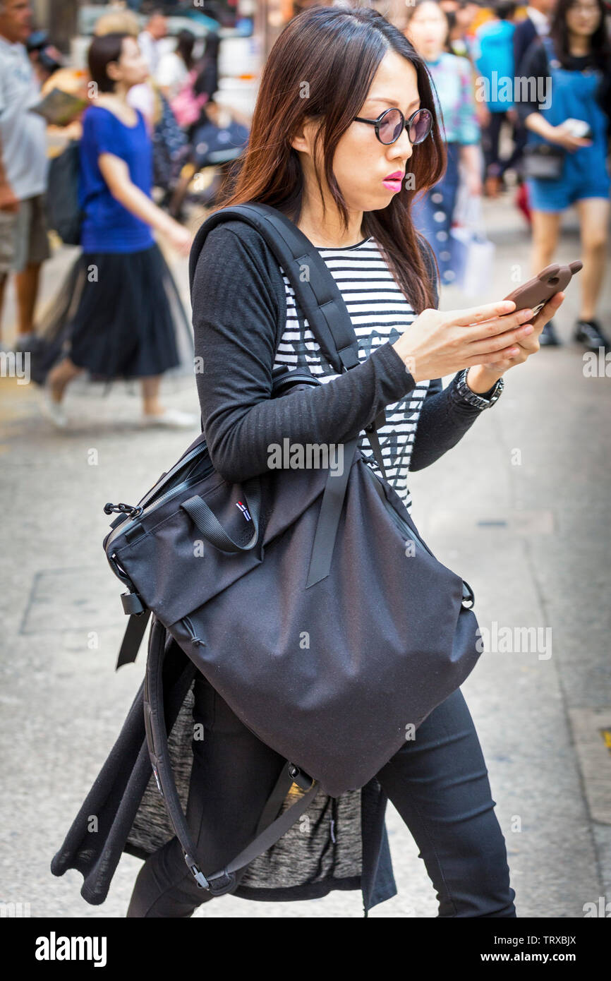 Asiatische Frau konzentriert sich auf mobiles Gerät, während der Überquerung der Straße in Hong Kong, SAR, China Stockfoto