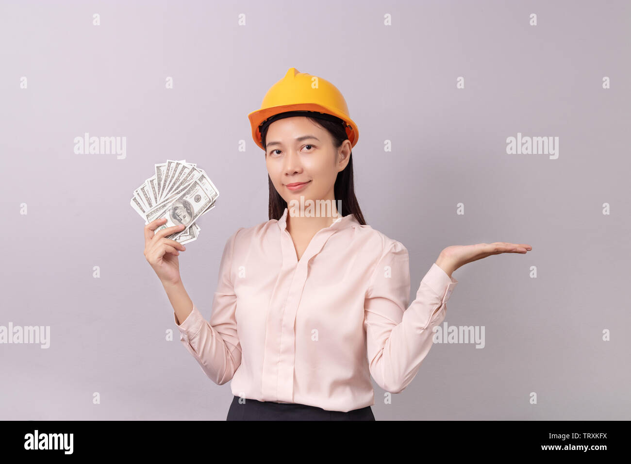 Kredite für Immobilien Konzept, Frau mit gelben Helm Holding banknote Geld in der rechten Hand und die leere Handfläche der linken Hand geöffnet Stockfoto